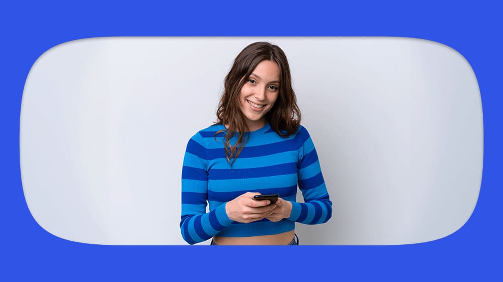 Jovem mulher sorridente usando blusa listrada azul, pesquisando no seu celular sobre hipoteca.