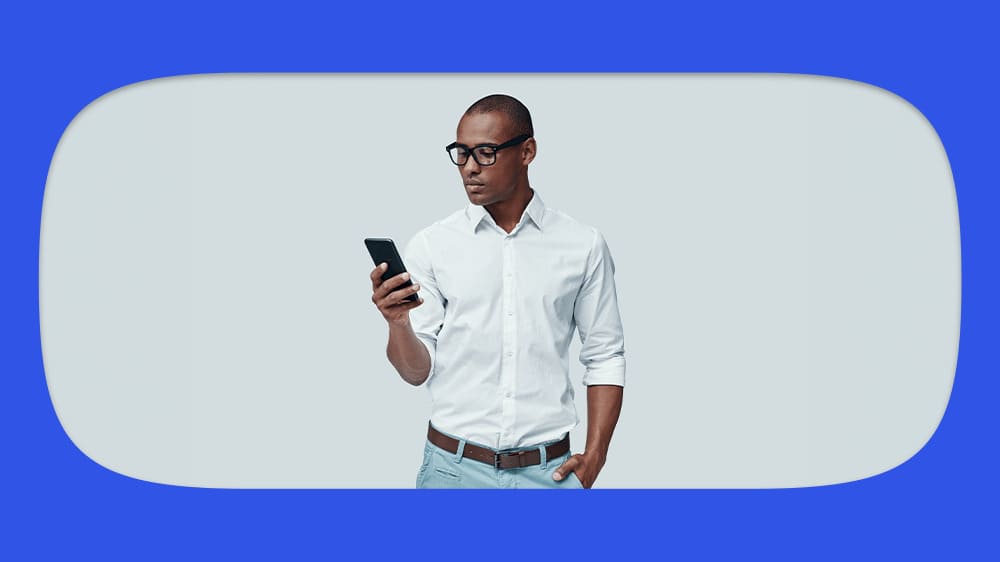 Homem jovem de óculos e camisa branca usando celular, consultando se seu nome está sujo.