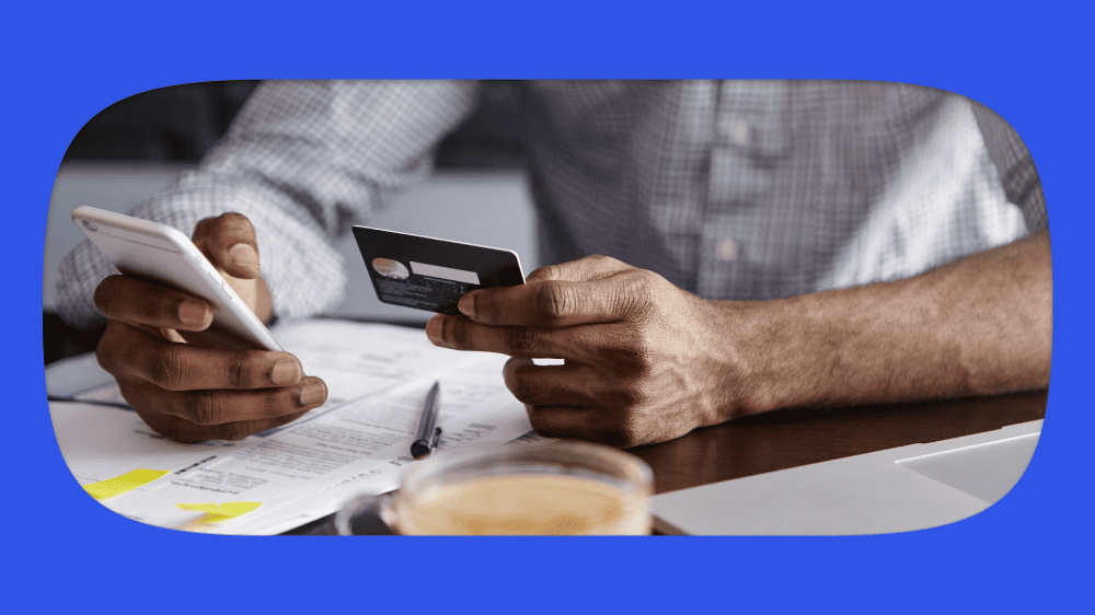 Pessoa com cartão de crédito na mão e um celular pesquisando se o banco pode tomar seus bens se não pagar o cartão de crédito