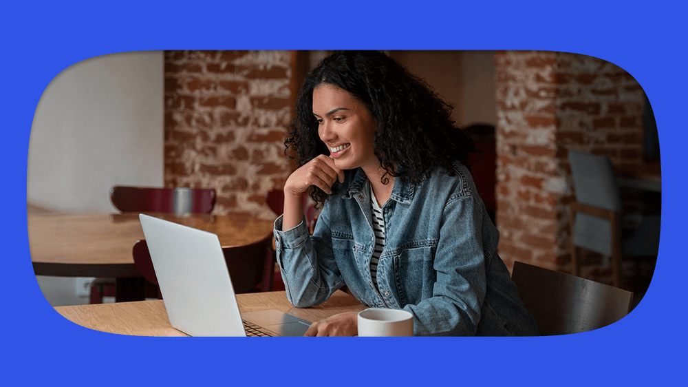 Mulher feliz usando notebook em ambiente moderno, com parede de tijolos ao fundo, consultando em seu notebook o fgts de conta invativa.