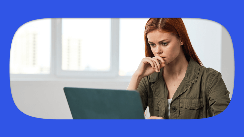 Mulher de cabelo vermelho pensando enquanto usa um notebook resolvendo CPF inconsistente no cadastro NIS, em um ambiente interno bem iluminado, com foco na expressão de concentração.
