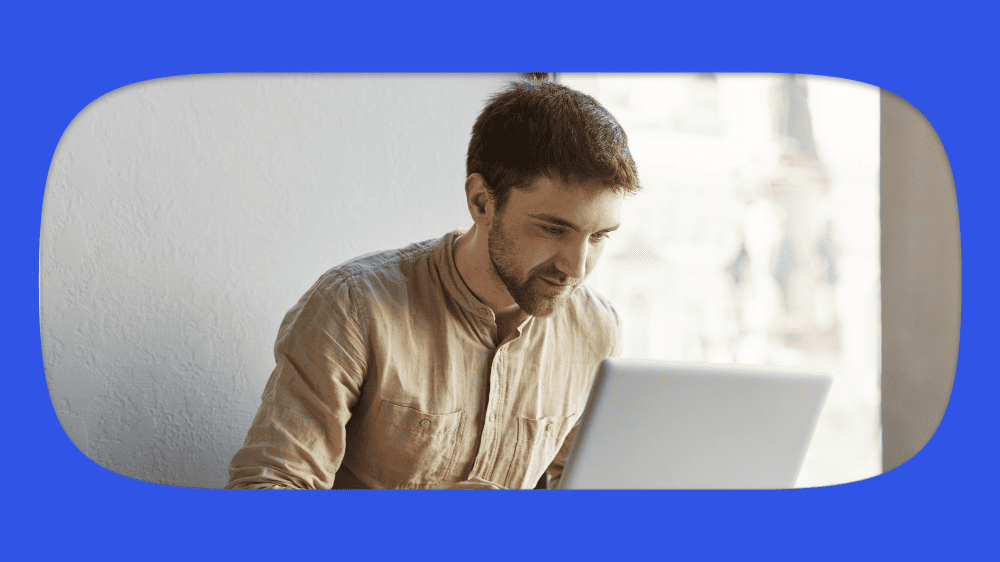Homem de cabelo castanho, barba leve, usando camisa bege, consultando como saber se o site é seguro em computador portátil em ambiente bem iluminado e moderno.