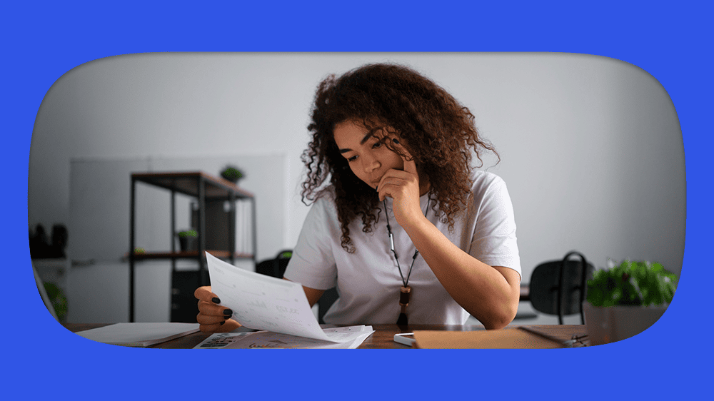 Mulher com cabelo cacheado lendo um documento sobre infidelidade financeira em uma mesa de escritório, ambiente profissional com prateleira e plantas ao fundo.