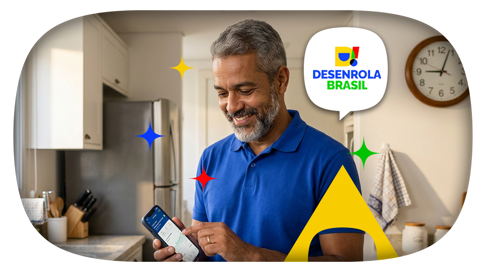 Homem de meia idade sorridente olhando para o celular, na cozinha de sua casa. Ao lado de seu rosto, surge o logo do programa Desenrola Brasil 2.0, com um elemento gráfico característico da identidade visual do programa logo abaixo.